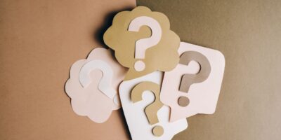 Question mark cutouts in layered paper craft style on a brown backdrop, conceptual art.